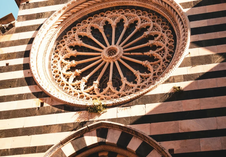 Ornate facade of a classic Italian church with striped design and intricate rose window in Liguria.
