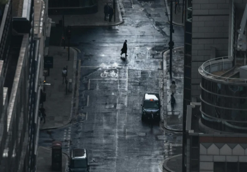 A dark, rainy street view of London with cars and a lone pedestrian under cloudy skies.