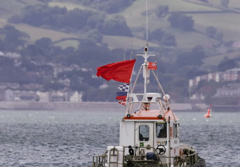 Small boat displaying flags navigating a scenic bay with a coastal backdrop.