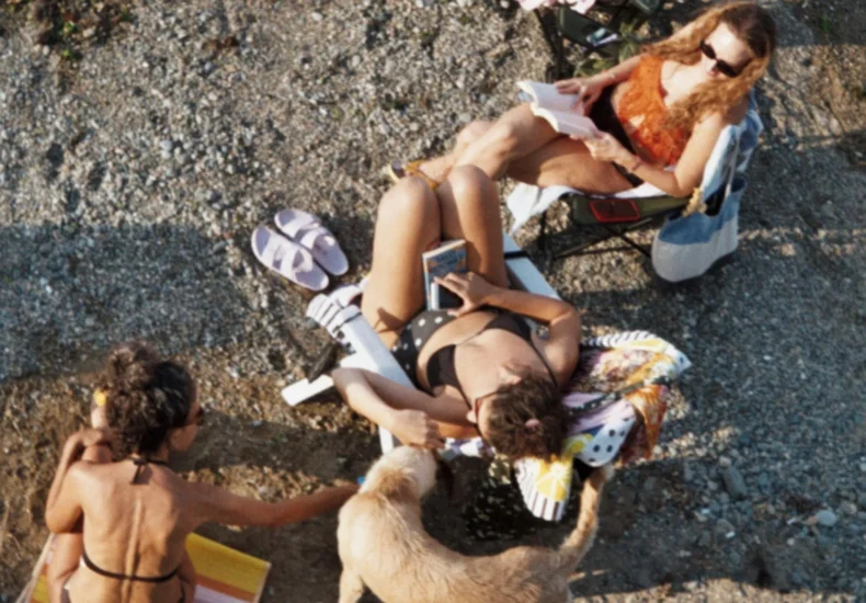 Group of women sunbathing on a pebble beach with a dog, enjoying a summer day.