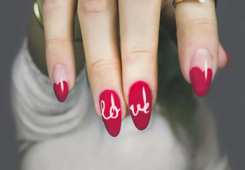 Vibrant red nails with 'love' art on a woman's hand, showcasing elegant style and design.