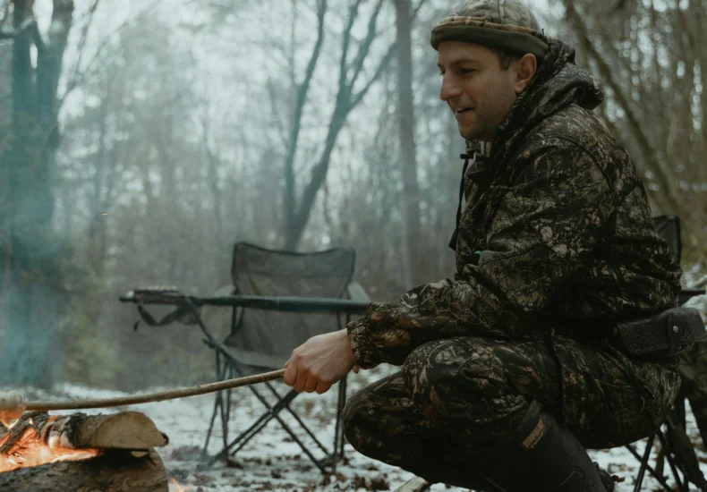 Man roasting food at a campfire in snowy forest, capturing winter adventure spirit.