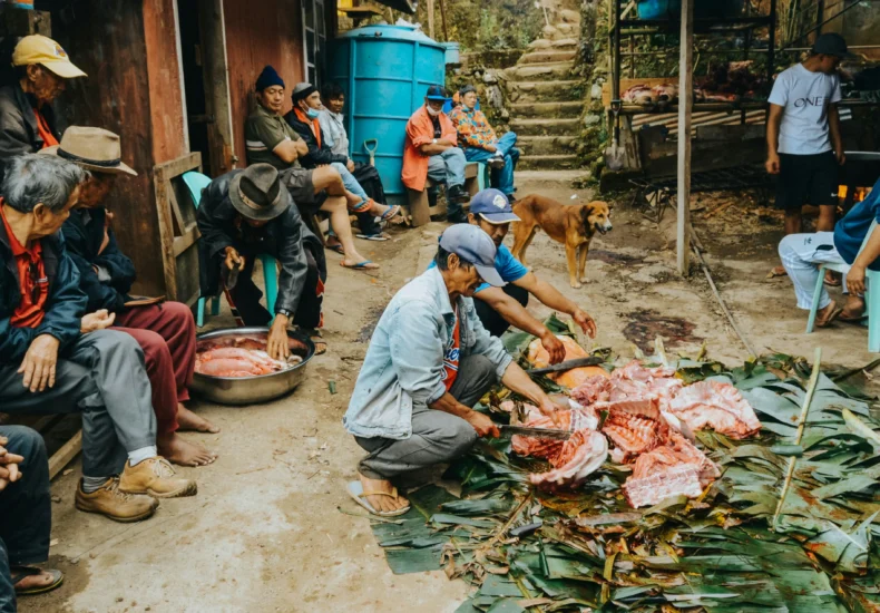 A group of villagers preparing meat in an outdoor setting, showcasing traditional methods and community spirit.