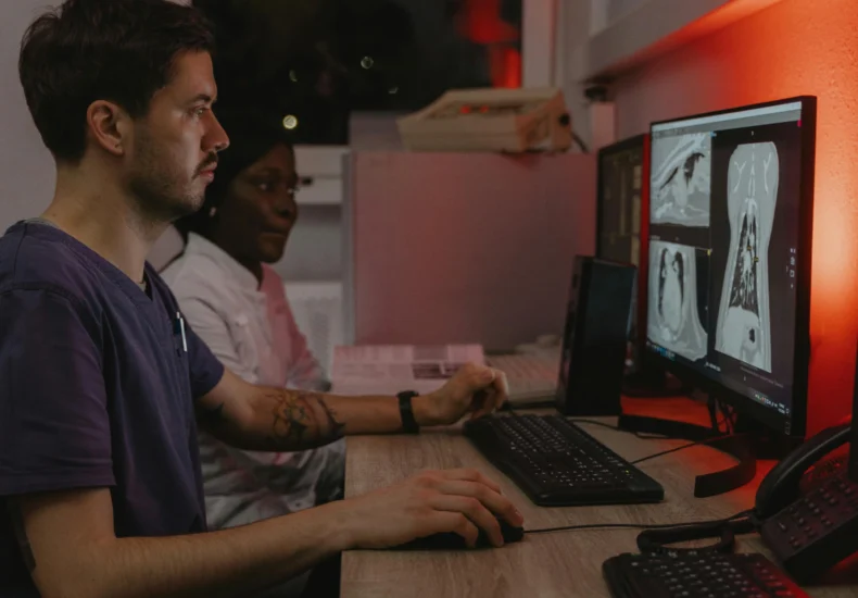 Two healthcare professionals working at computers analyzing medical scans in a clinical setting.