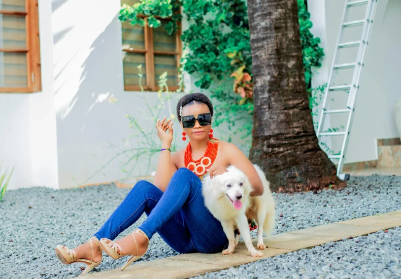 Fashionable woman sitting with her dog in a sunny outdoor setting, exuding style and elegance.