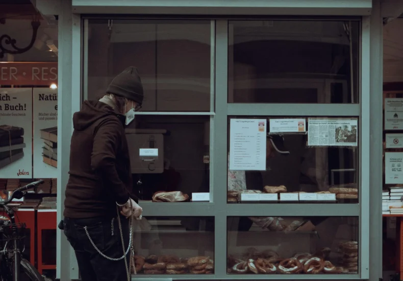 A person with a dog stands by a pretzel shop, contemplating a purchase.