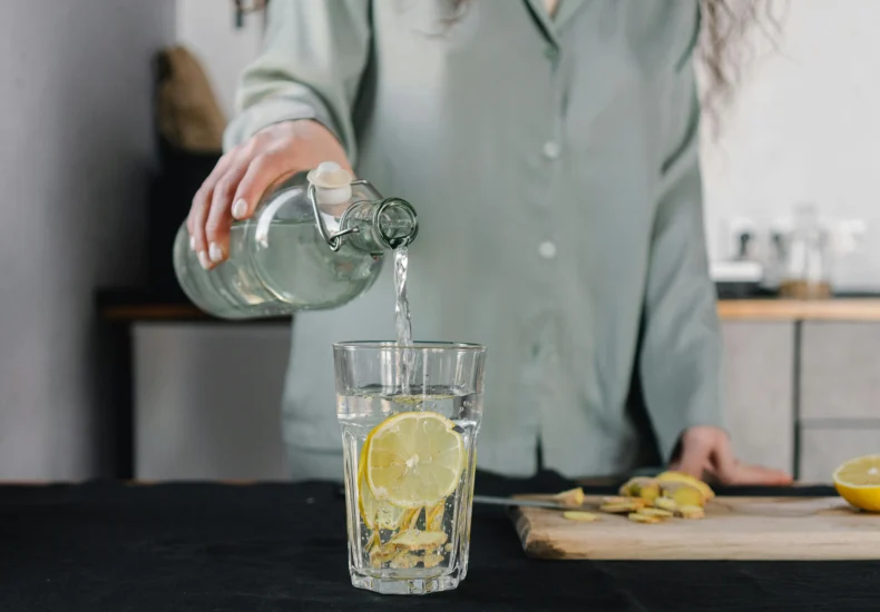 Woman pours water for lemon ginger infusion, promoting health and hydration.