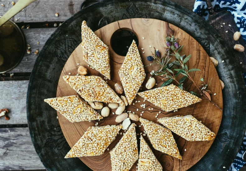 Close-up of diamond-shaped sesame seed and peanut brittle on a rustic wooden plate.