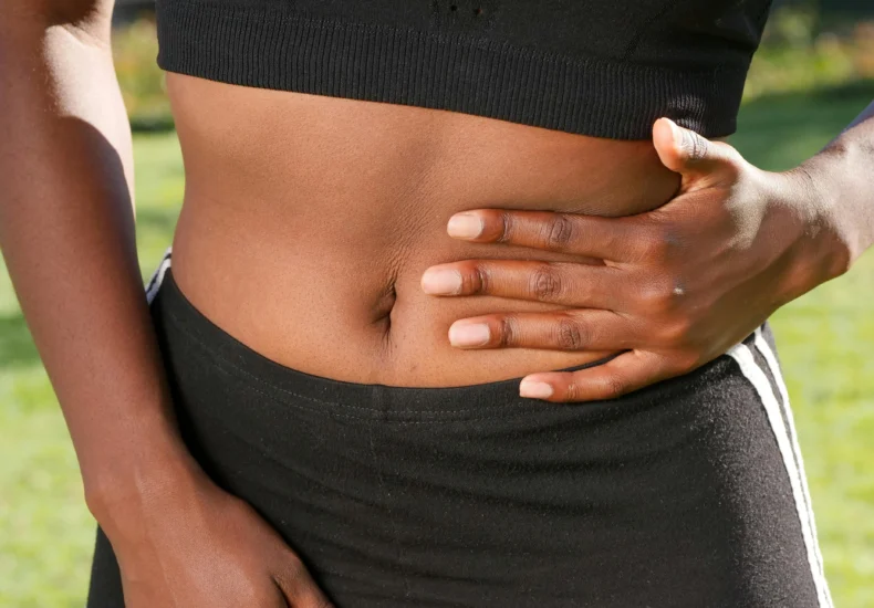 Close-up of a person holding their abdomen, indicating stomach discomfort, outdoors.