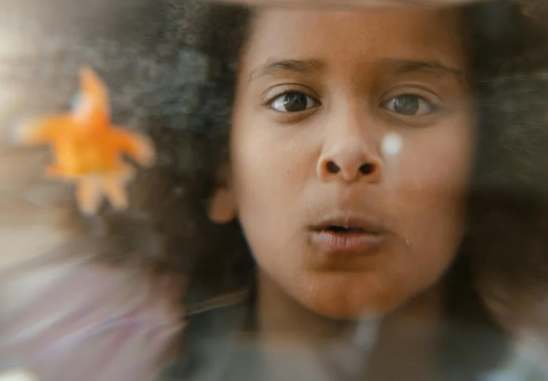 Child with an amazed expression looking through glass with a fish in focus.