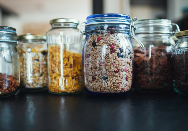 Close-up of various cereals in glass jars on a kitchen counter, showcasing diverse breakfast options.
