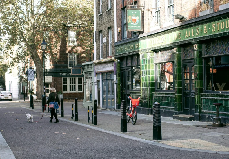 Woman walking dog past traditional pub on a quiet street, capturing urban charm.