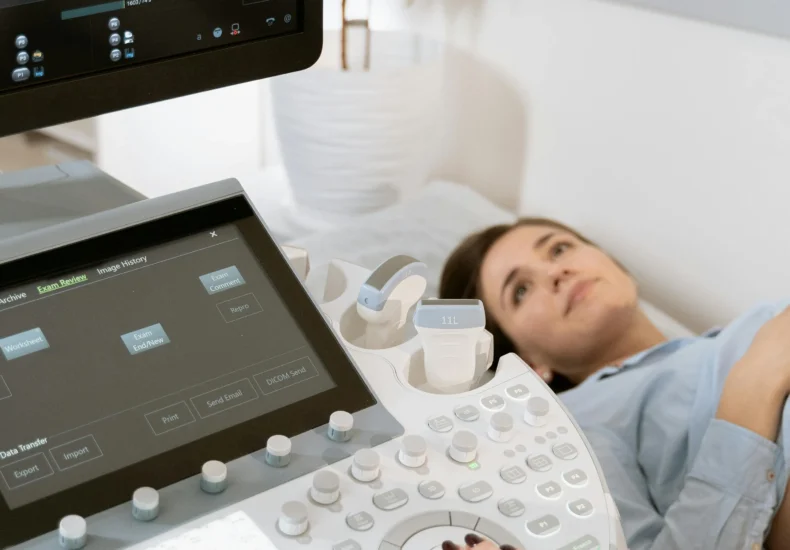 Pregnant woman undergoes ultrasound scan by medical professional in hospital room.