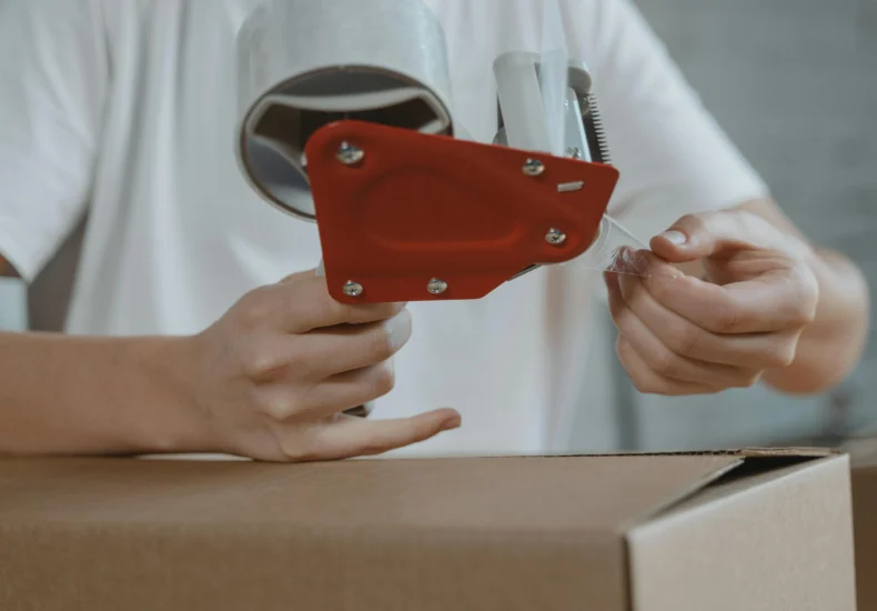 Close-up of person sealing a cardboard box with tape for packaging and shipping.