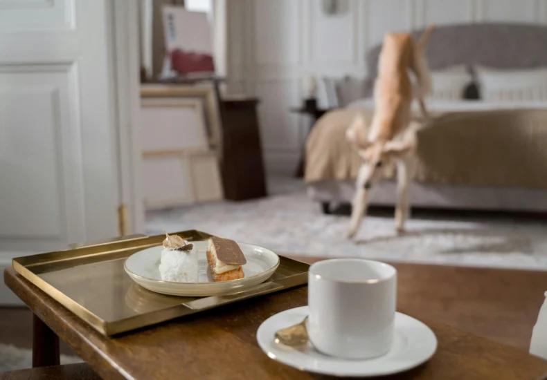 Serene bedroom with coffee, dessert, and a playful dog creates a warm home vibe.