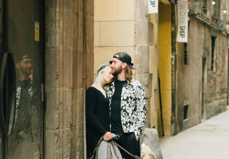 A couple shares a kiss in a quaint European alley with their dog. Cozy, romantic mood.