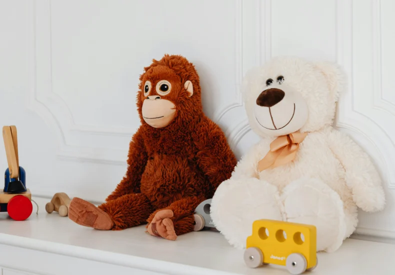 Cute plush teddy and monkey toys with wooden cars on a white shelf, perfect for kids' room decor.