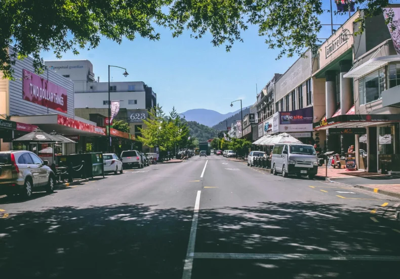 Wide street view in Nelson, New Zealand, with shops, cars, and a mountain backdrop.