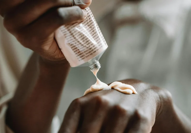 A close-up of hands applying skin care cream from a tube, emphasizing daily skincare routine.