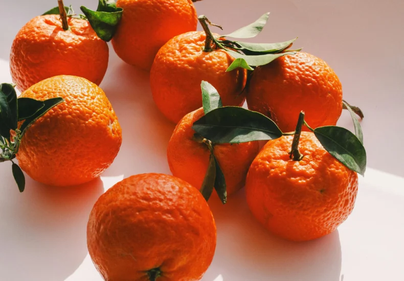 Fresh oranges arranged in sunlight casting intricate shadows, showcasing vibrant texture.