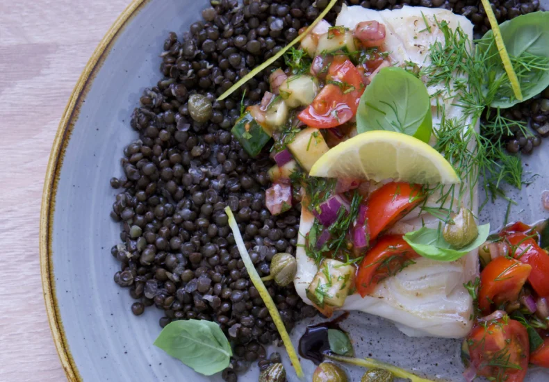 Close-up of a delicious cod fish dish with lentils, salsa, and fresh herbs on a plate.