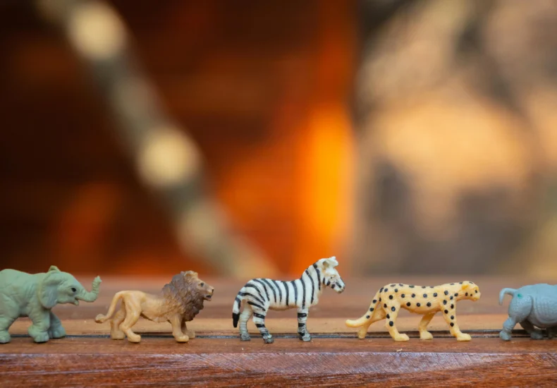 Miniature toy animals in a row on wood, displaying various wild species.
