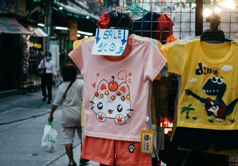 Children's clothing with cartoon designs displayed for sale in a vibrant street market during the night.