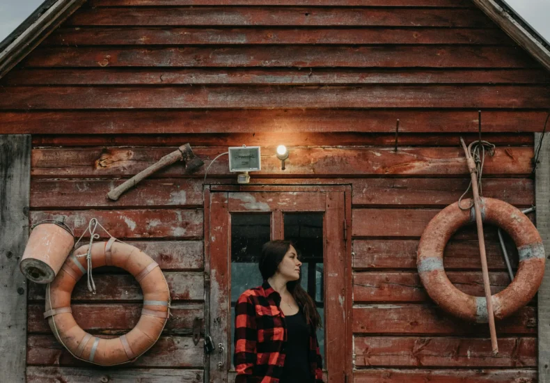 A rustic wooden cabin with a woman and her dog standing outside, evoking a sense of adventure and warmth.