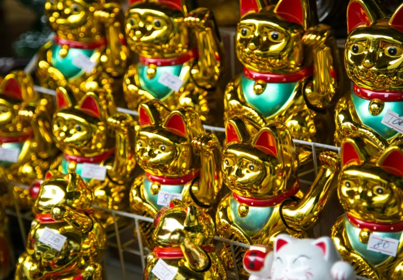 Golden Maneki-neko figurines on display in a market setting in Bangkok, Thailand.