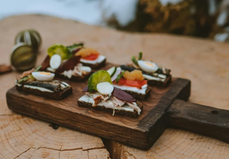 Appetizing open sandwiches on a rustic cutting board displayed on a tree stump outdoors in winter.