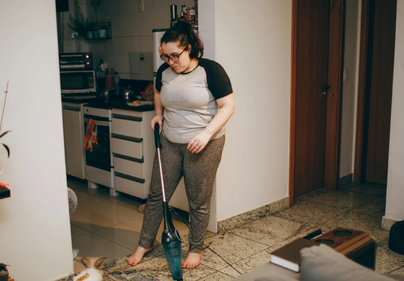 A woman cleaning her living room with a vacuum cleaner while her pet rabbit watches.