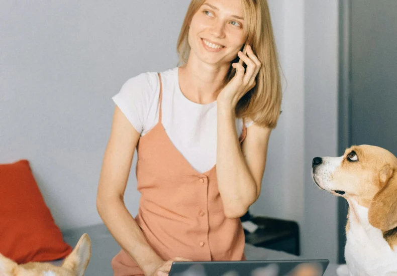 Smiling woman working on laptop with dogs at home, enjoying remote work on bed.